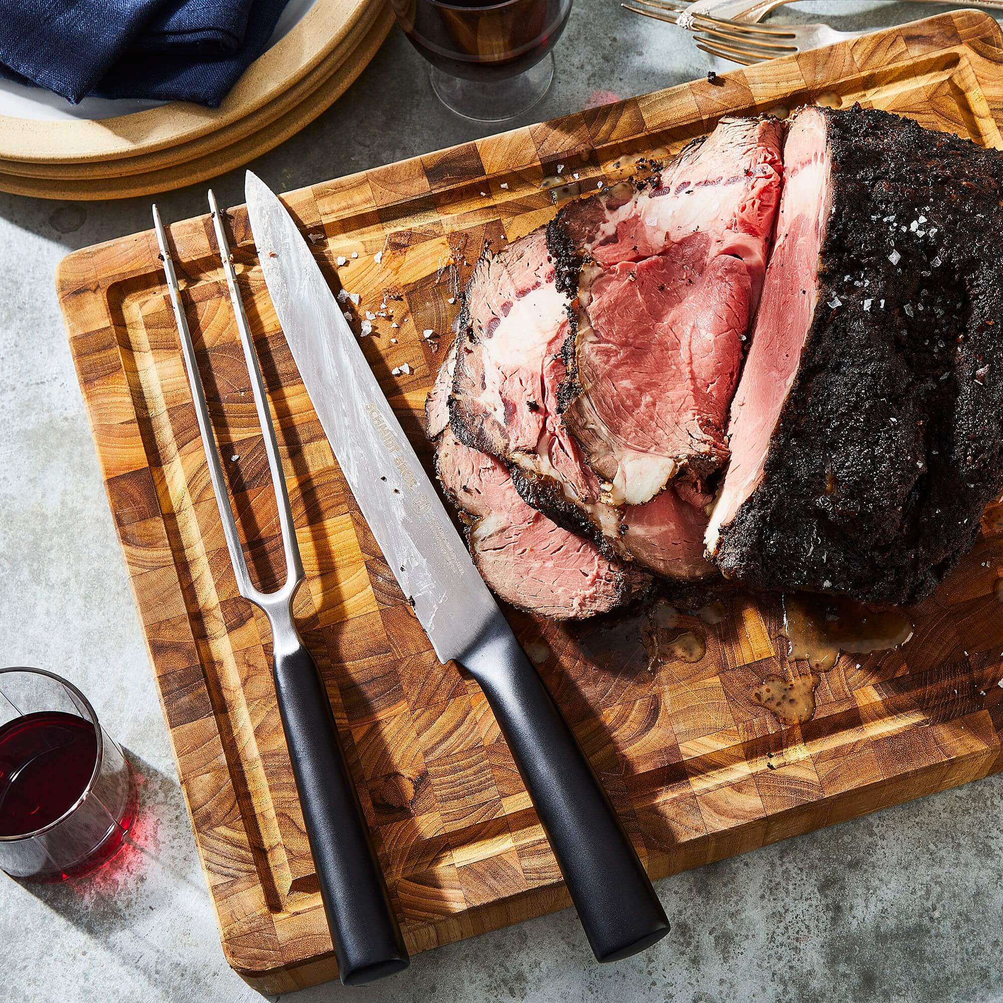 Sliced grilled flank steak with knife and fork on a wooden cutting board, accompanied by a glass of red wine.