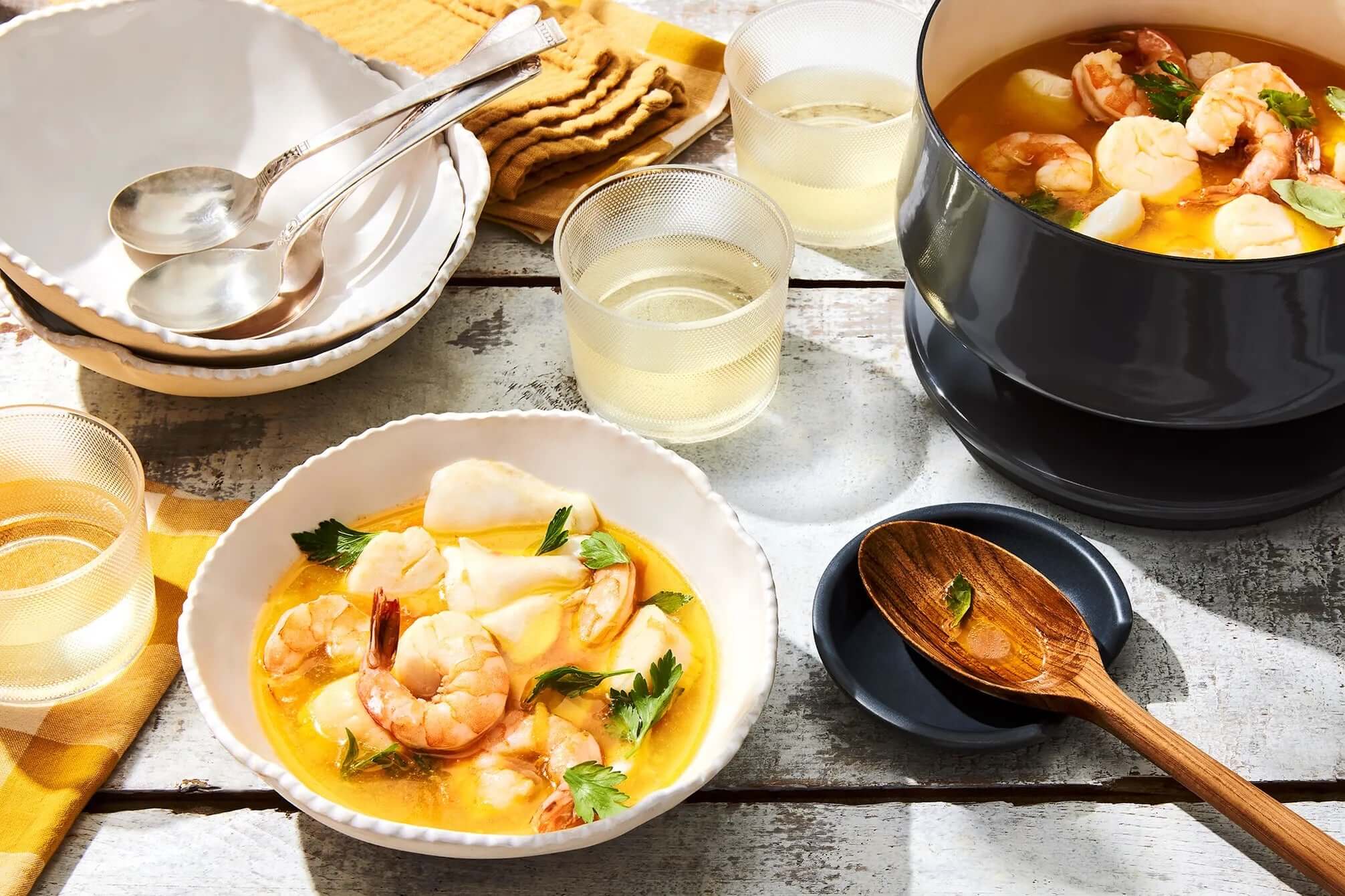 Classic bouillabaisse served in white bowls with shrimp and fish, accompanied by glasses of white wine on a rustic table.