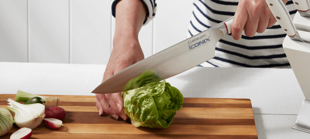 Slicing lettuce with a chef's knife on a wooden cutting board.