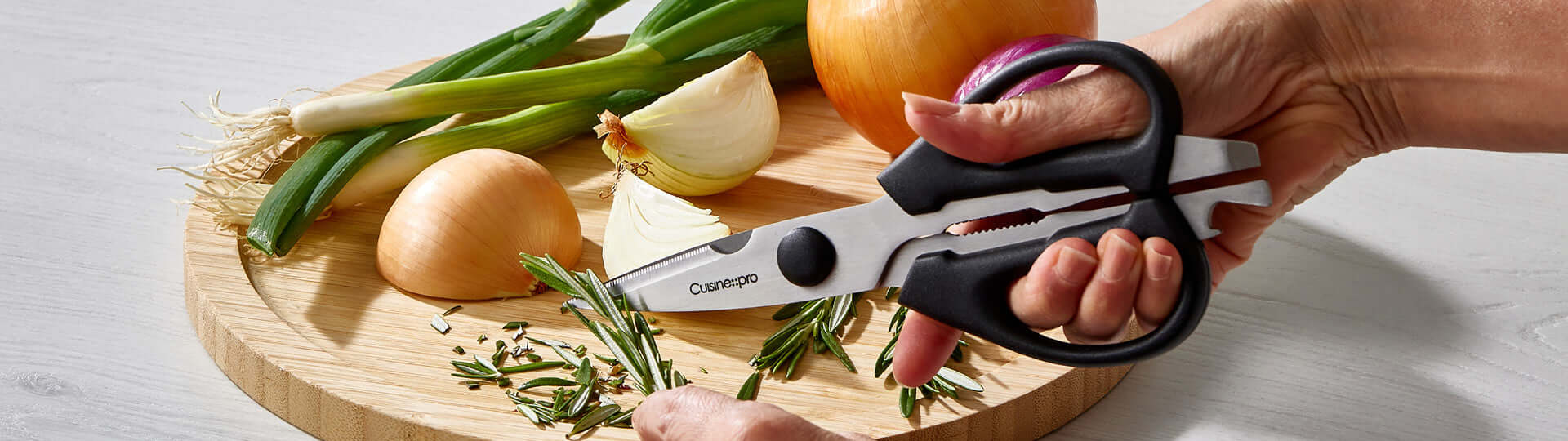 Ergonomic kitchen shears cutting fresh herbs on a wooden cutting board with onions and green onions.