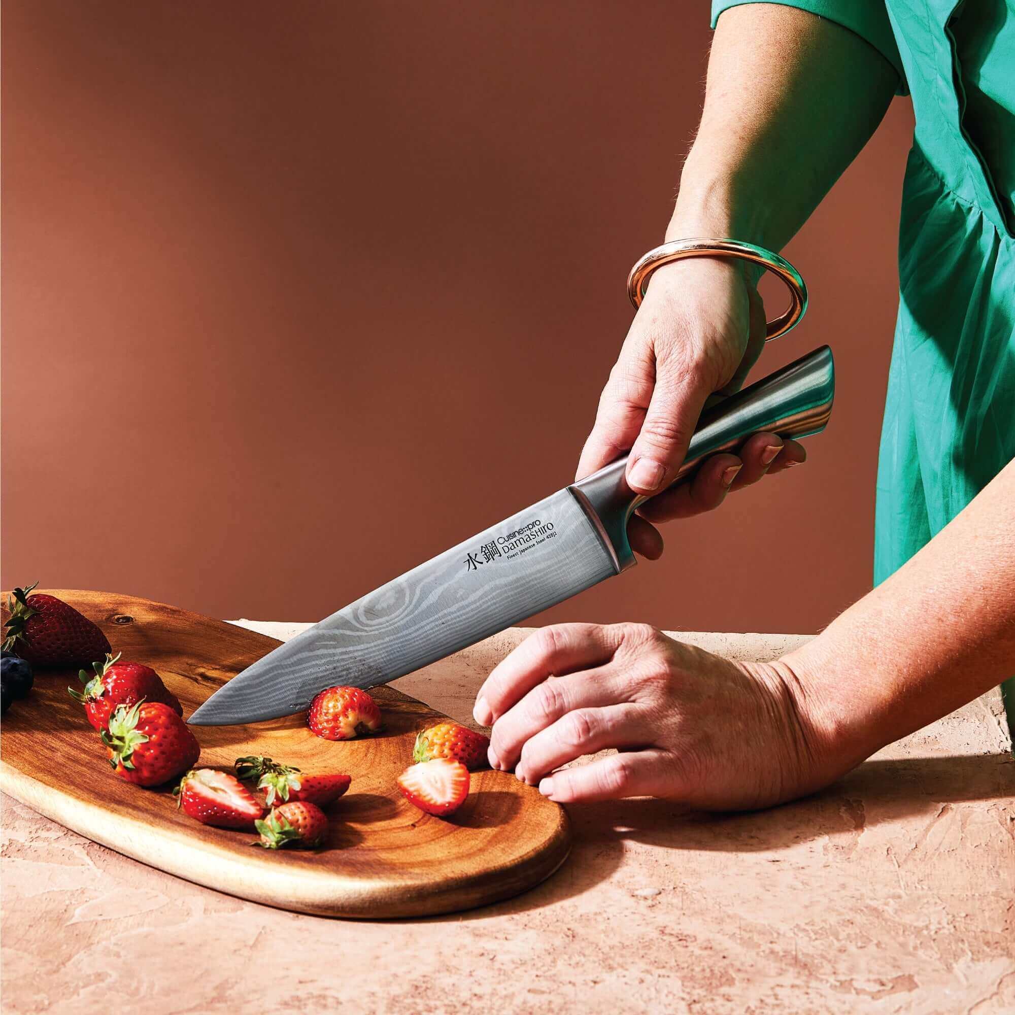 Person using Cuisine::pro® Damashiro® Meiyo Knife to slice strawberries on a wooden board.