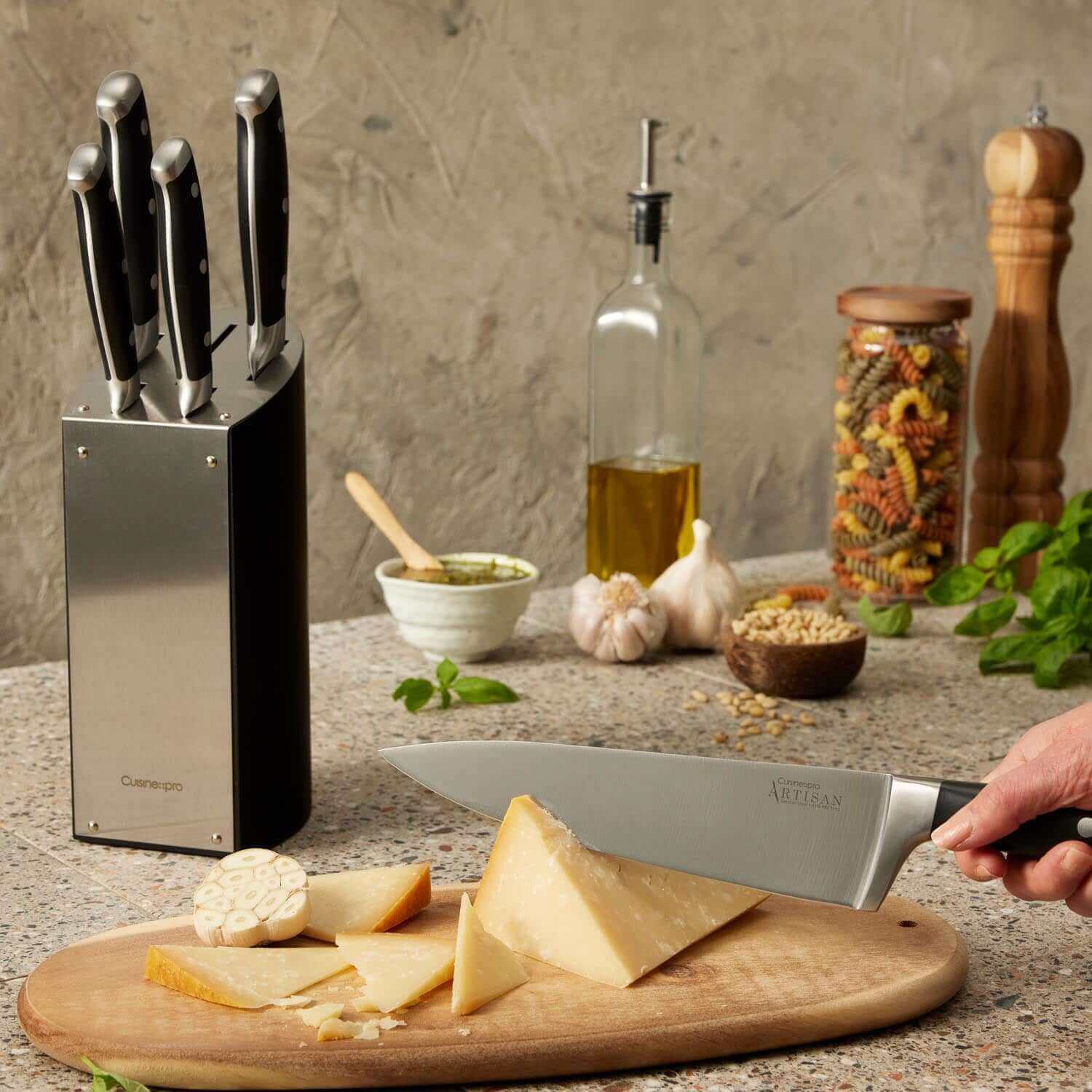 Cuisine::pro® ARTISAN™ Kyoto Knife Block 6 Piece set in a kitchen with assorted food items and a chef slicing cheese